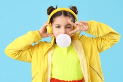 Trendy Girl Blowing Bubble Gum While Showing Victory Gesture On Blue Background