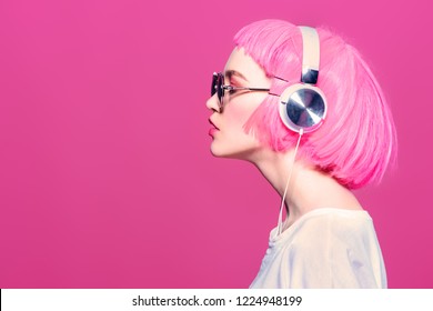 Trendy girl with pink hair wearing sunglasses enjoys the music on headphones. Pink background. Youth style, leisure. - Shutterstock ID 1224948199