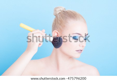 Trendy girl posing with professional make-up brush isolated on blue background
