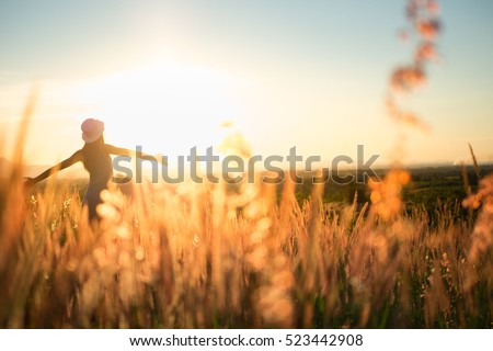 Trendy girl in stylish summer dress with beautiful hat walking in the field with flowers in sunlight