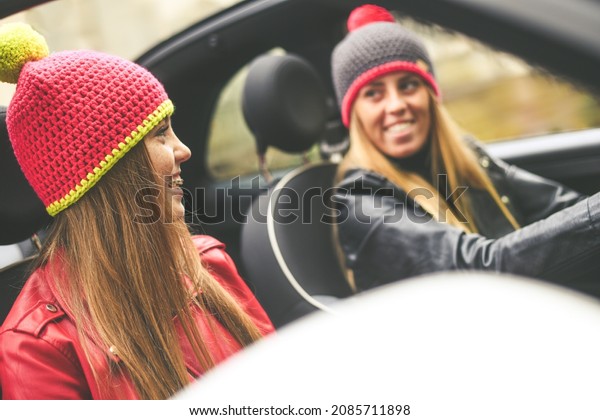 Trendy girls sitting in the car. Smiling teen in\
front of the steering wheel with a friend beside. Young women\
enjoying free time wearing leather jacket in a convertible car.\
Youth, freedom concept.