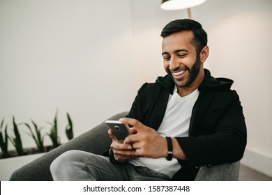 Trendy Handsome Gen Z Indian Arabic Man Typing On Mobile Phone, Smiling And Laughing