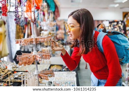 Trendy hipster asian woman looking for fancy jewelry and accessories in a flea market shop
