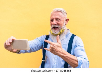 Trendy hipster man using mobile phone doing video call while wearing fashion silk safety mask - Outfit, technology and lifestyle during coronavirus time - Focus on face - Powered by Shutterstock