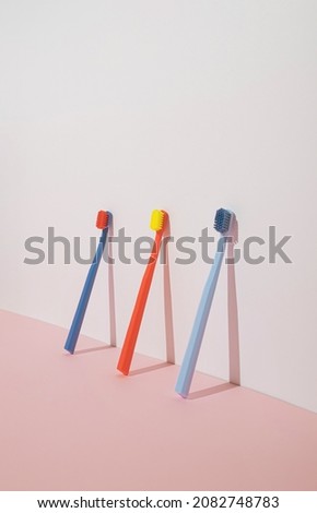 Trendy minimal composition with three colourful toothbrushes on pastel pink background. Modern aesthetic.