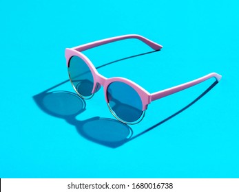 Trendy minimal style photography of  pink sunglasses on pastel blue background. Minimalist summer fashion or vacation concept. Sunny and vivid background with hard light and shadow.
