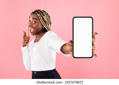 Trendy Mobile Phone. Excited young black lady holding smartphone with white empty screen in hand, showing device close to camera. Gadget with blank space, mockup, selective focus, blurred background