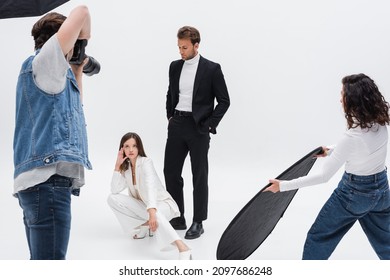 trendy models posing near photographer and assistant with reflector on white