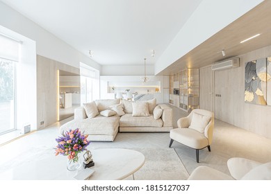 trendy modern interior design of a large studio in white and beige colors with large floor-to-ceiling windows. area of ​​white kitchen with an island and a recreation area