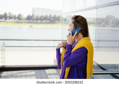 Trendy Modern Mature Redhead Woman Chatting On Her Mobile Outdoors On A Patio Looking Away From The Camera Out Over A High Key Cityscape With Copyspace