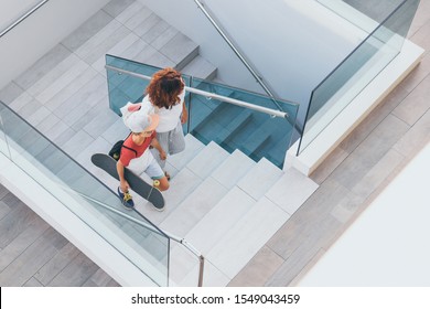 Trendy mother and son walking on stairs in a modern city context. Young boy with skateboard goes up the ladder with mum. Top view of people walks in a modern mall. Family scene at the shopping center - Powered by Shutterstock