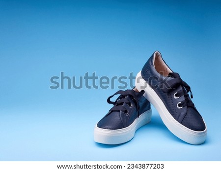 Trendy navy blue sneakers isolated on the gradient blue background. Perforated leather, metal eyelets, thick shoelace, white rubber sole. Stylish minimalism footwear concept