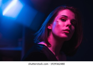 Trendy Night Portrait Of A Beautiful Woman With Beautiful Makeup In The Style Of Euphoria, Posing In A Dark Room In Neon Light, Looking At The Camera.