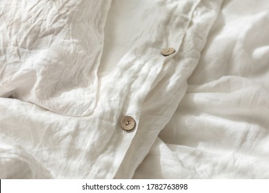 Trendy organic natural linen bedclothes with wooden buttons closeup. Bedding, morning light, bedroom style and design. Rough textile background with wrinkle.