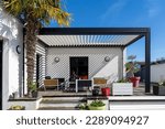 Trendy outdoor patio pergola shade structure, awning and patio roof, garden lounge, chairs, metal grill surrounded by landscaping