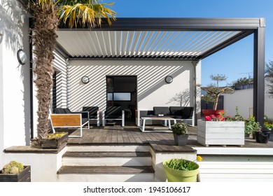 Trendy outdoor patio pergola shade structure, awning and patio roof, garden lounge, chairs, metal grill surrounded by landscaping - Shutterstock ID 1945106617