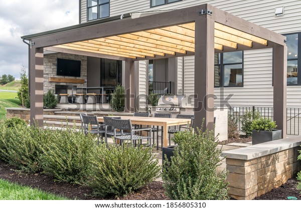Trendy outdoor patio pergola shade structure,\
awning and patio roof, dining table, chairs, metal grill surrounded\
by landscaping