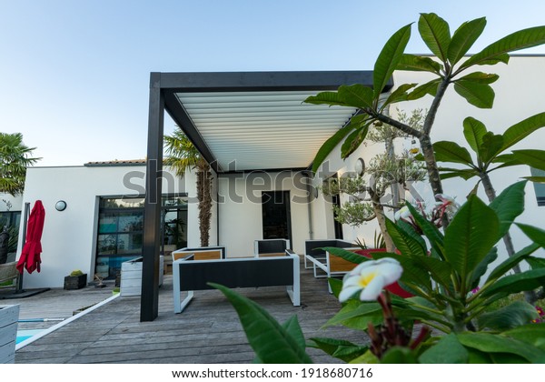 Trendy outdoor patio pergola shade structure,\
awning and patio roof, garden lounge, chairs, metal grill\
surrounded by\
landscaping