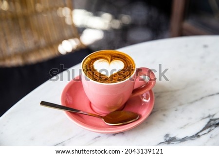 Trendy pink cup of hot cappuccino on marble table background. Heart shape latte art for symbol of love. One cup for morning routine.