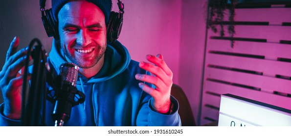Trendy podcast creator streaming audio broadcast at his home studio using stylish cyber punk blue magenta ambient light