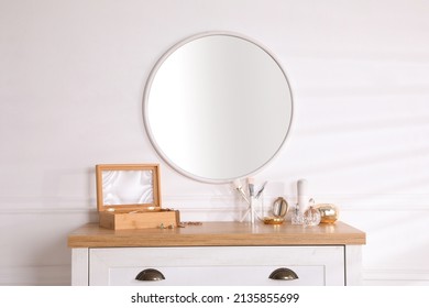 Trendy Round Mirror And Chest Of Drawers With Accessories Near White Wall Indoors.