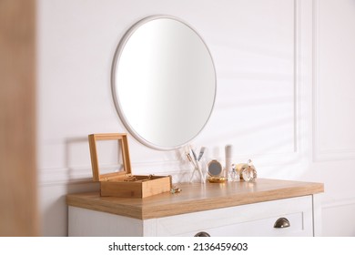 Trendy Round Mirror And Chest Of Drawers With Accessories Near White Wall Indoors.