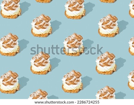 Trendy seamless pattern made with cream puffs on blue background. Minimal food concept. Cream puffs filled with pastry cream and sprinkled with powdered sugar.