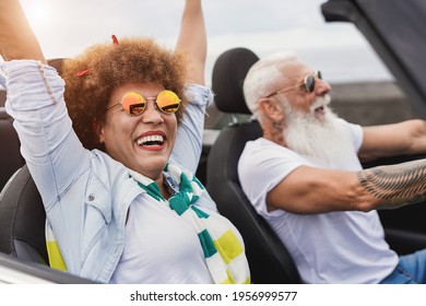 Trendy senior couple having fun inside convertible car - Multiracial mature people on a road trip with cabriolet car