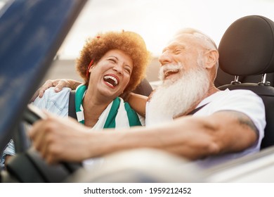 Trendy senior couple having fun inside convertible car - Multiracial mature people on a road trip in summer vacation with cabriolet car - Powered by Shutterstock