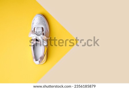 Trendy sequin sneaker with white satin shoelaces isolated on a geometric yellow-beige background with pointing on copy space. Flat lay. Creative layout with footwear. Outlet marketing poster.
