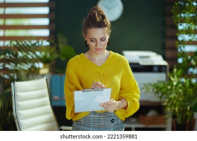 Trendy Small Business Owner Woman In Yellow Sweater With Clipboard In The Modern Green Office.