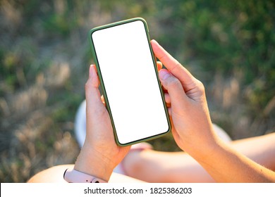 Trendy smartphone device mock up. Hipster girl holding mobile phone with blank screen with copy space for design or logo outdoors, sunny weather