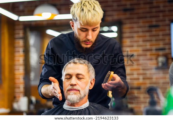 trendy stylish master cuts hair of old man\
client in modern\
barbershop