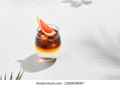 Trendy summer drink - espresso tonic on white background with shadow of sun. Cold coffee cocktail in summer sunny day. Coffee menu. Aesthetic composition with iced espresso and tonic cocktail
