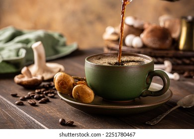 Trendy superfood mushroom coffee is pouring in green cup on wooden background. Healthy concept with copy space, selective focus.