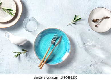 Trendy tableware with a blue plate, shot from the top. Dinnerware set for dinner, with olive branches for decor, Mediterranean food concept. Elegant dishes, overhead flat lay shot