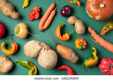 Trendy ugly organic vegetables. Assortment of fresh eggplant, onion, carrot, zucchini, potatoes, pumpkin, pepper in craft paper bag over green background. Top view. Cooking ugly food concept. Non gmo