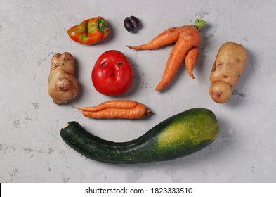 Trendy Ugly Organic Vegetables: potatoes, carrots, tomato, pepper, zucchini and plum on gray background, ugly food concept, top view