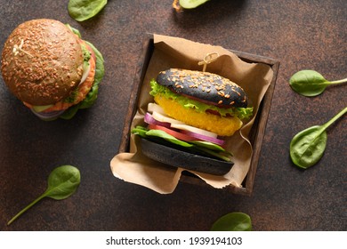 Trendy Vegan Burger Of Black Charcoal Buns, Vegetables, Cabbage And Carrot Meatball As Plant Based Meat On Black Table. View From Above.