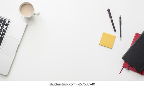 Trendy White Office Desk From The Above With Coffee And Work Related Items On It: Notebook, Pens, Macbook