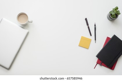 Trendy White Office Desk From The Above With Coffee And Work Related Items On It: Notebook, Pens, Macbook