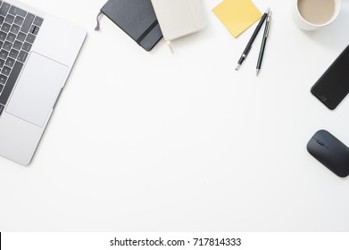 Trendy White Office Desk From The Above With Coffee, Phone, Mouse And Work Related Items On It: Notebooks, Pens, Sticky Notes, Laptop