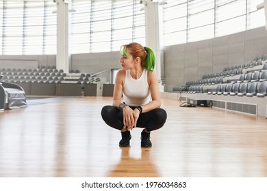 Trendy Woman Athlete Crouching Down Looking To The Side Of Empty Indoor Stadium Arena With Bright Sunlight Shining In. Motivational And Inspiring Athlete Before Competition