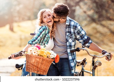 Trendy young couple stop to riding on their bike with basket of flowers while focused on hug.