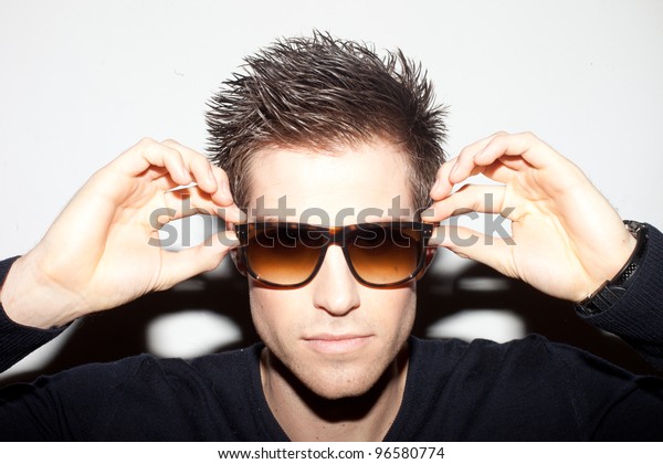Trendy young man with spiky hair with his\
hands raised to a pair of\
sunglasses.