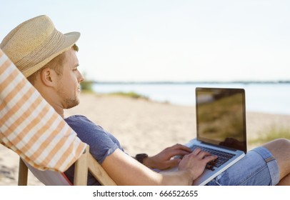 Trendy Young Man Using A Laptop At The Beach