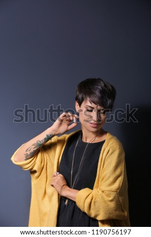 Trendy young woman with tattoo on grey background