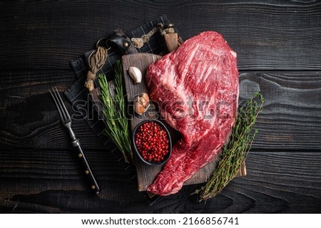 Tri Tip black angus beef steak on cutting board with herbs, raw meat. Black Wooden background. Top view.