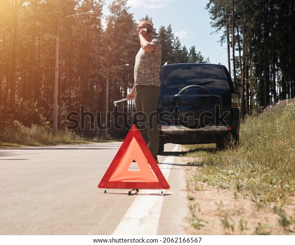 Triangle\
caution warning sign on road side after car break and driver\
speaking on phone, calling for repair\
service.