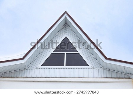 Triangle gable window on white house roof, highlighting geometric symmetry, clean lines and minimalist architectural detail. Home design, real estate and architecture projects.